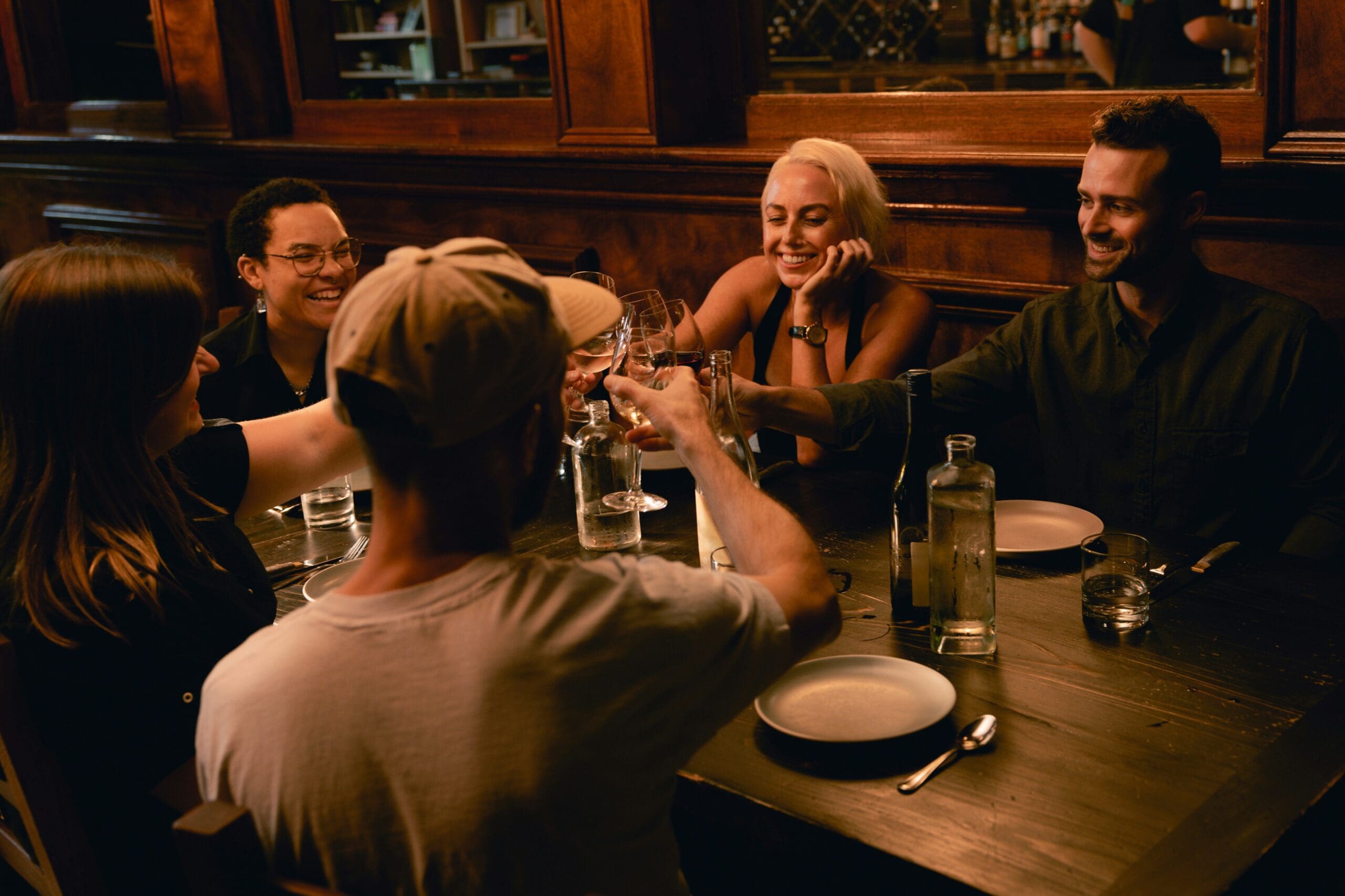 five people seated at a dimly lit table laughing and clinking drinks