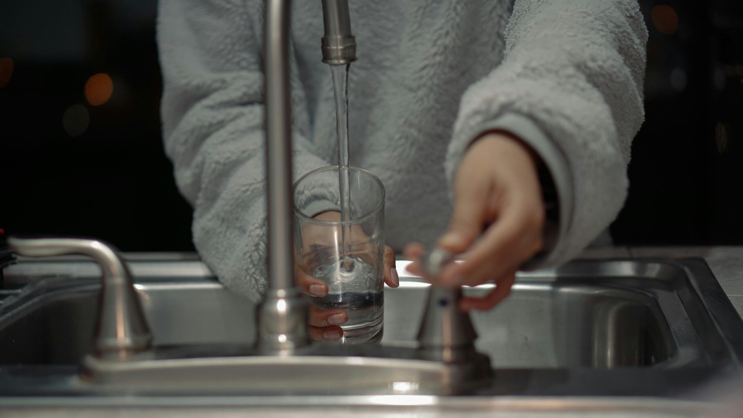 person wearing a light grey sweater putting tap water into a glass